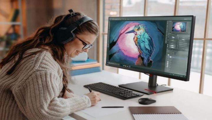 Una mujer sonríe mientras trabaja, sentada en un escritorio con el monitor Lenovo ThinkVision.
