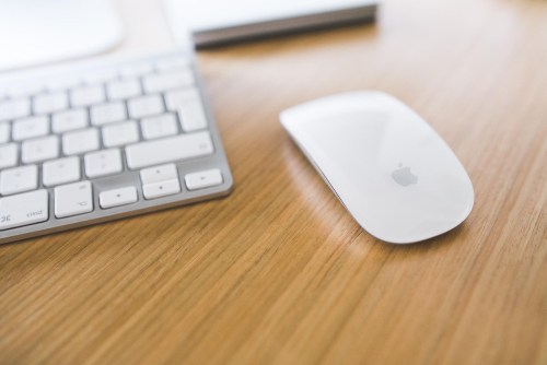 Magic Mouse next to a Mac keyboard on a desk.
