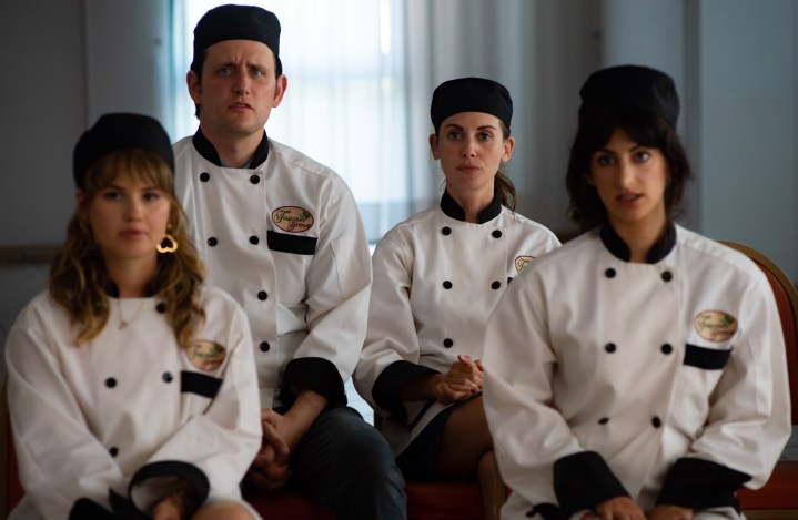 Debby Ryan, Zach Woods, Ayden Mayeri, and Alison Brie sit in their chef gear and look on in a scene from Spin Me Round.