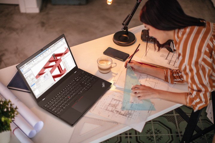 A designer sits by a desk as she works on a project with the Lenovo ThinkPad 15v next to her.