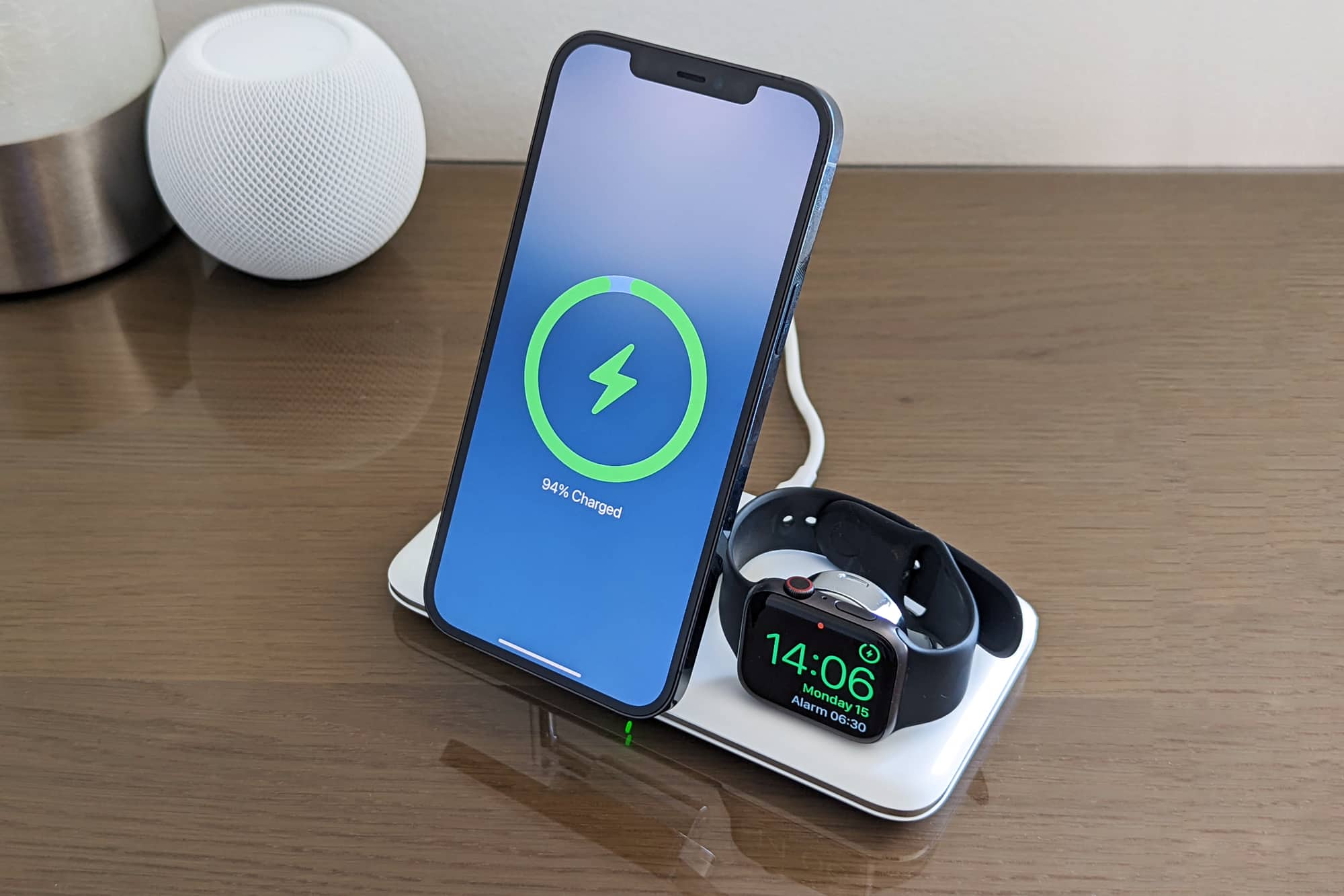 iPhone 12 Pro Max و Apple Watch Series 5 روی پایه شارژ Ugreen 3-in-1 MagSafe با HomePod mini در پس زمینه شارژ می شوند.