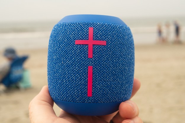 A hand is holding the Wonderboom 3 speaker in front of a beach background.