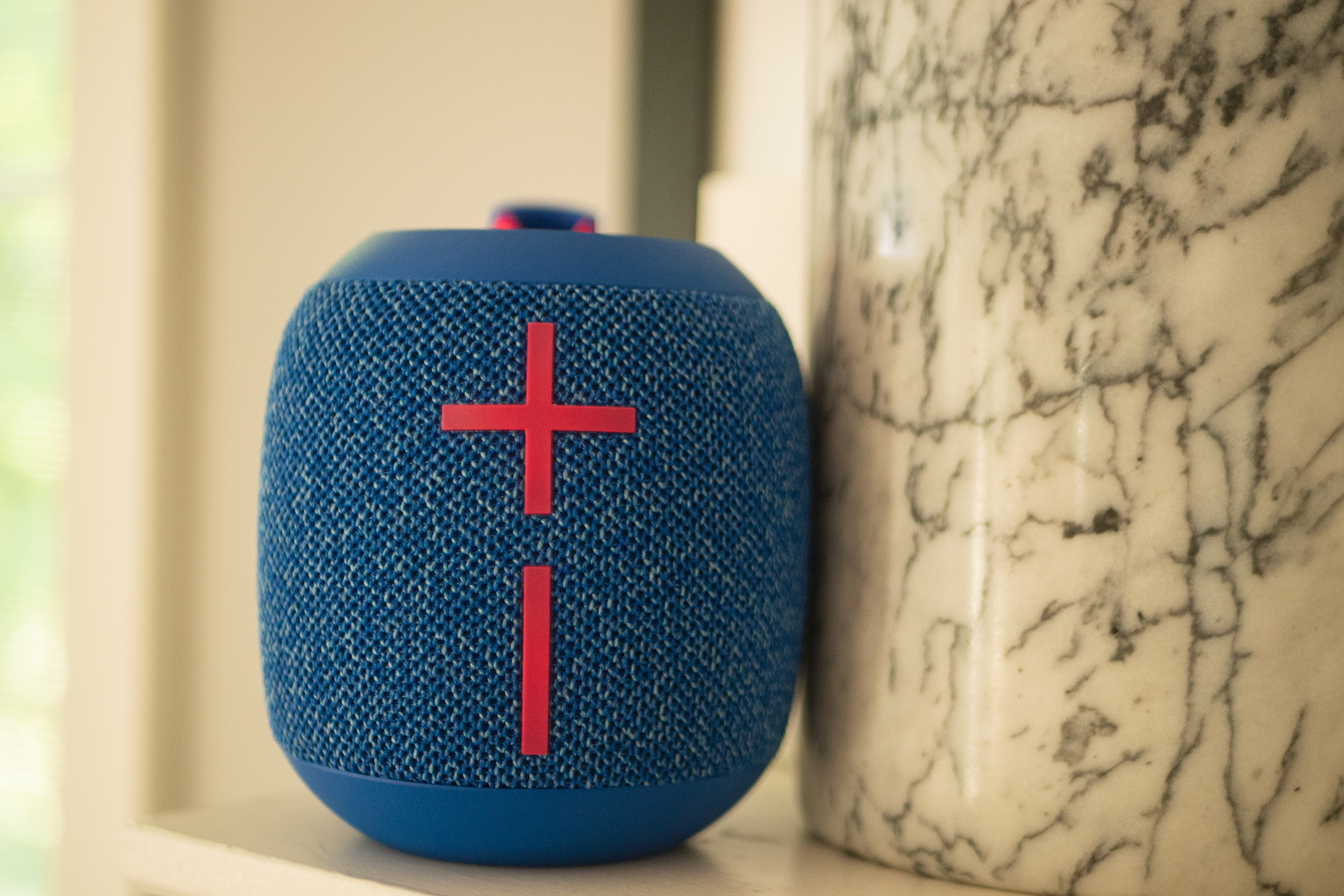 A Wonderboom 3 speaker is sitting on a mantle next to a marble-patterned container.