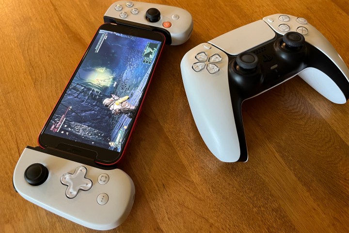 A DualSense controller sitting on a table next to a DualSense Backbone displaying the PS5 exclusive game Returnal on its screen.
