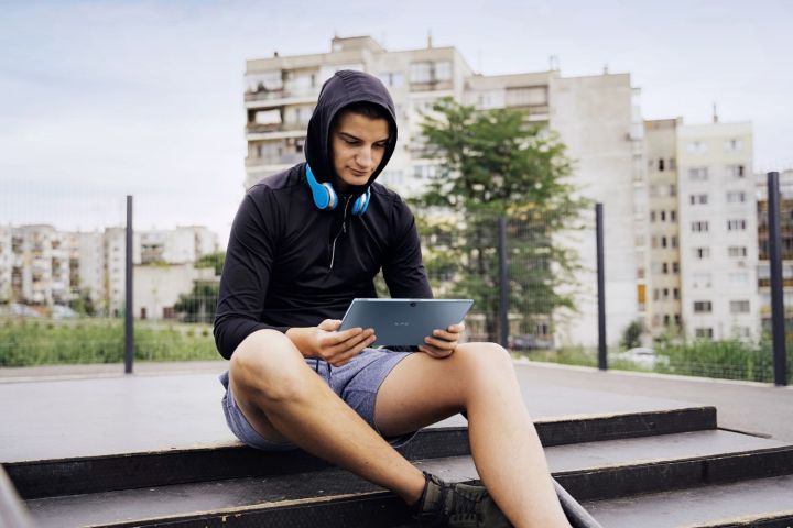 Ein junger Mann sitzt auf einer Außentreppe und hält das Dell XPS 13 2in1 in der Hand.