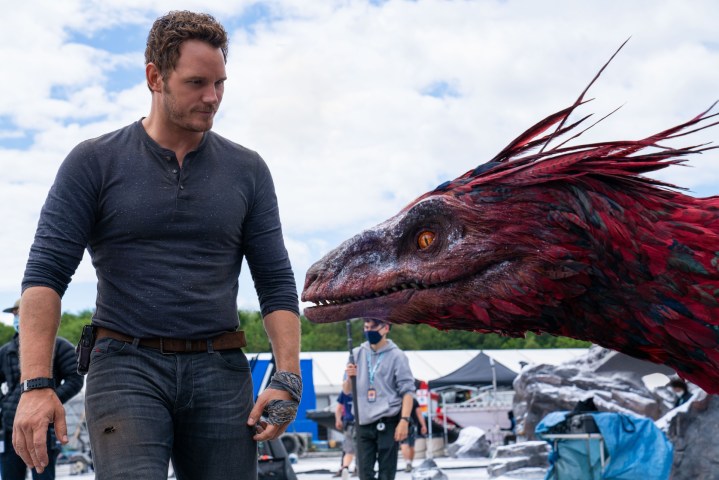 Chris Pratt stands next to a head model of a Pyroraptor on the set of Jurassic World Dominion.