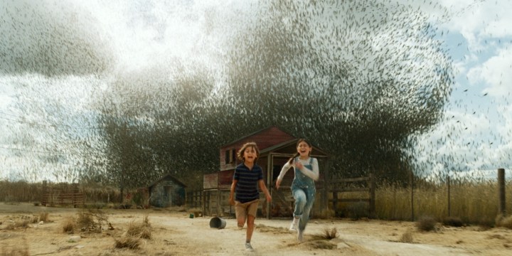 Duas crianças correm de um enxame de gafanhotos em uma cena de Jurassic World Dominion.