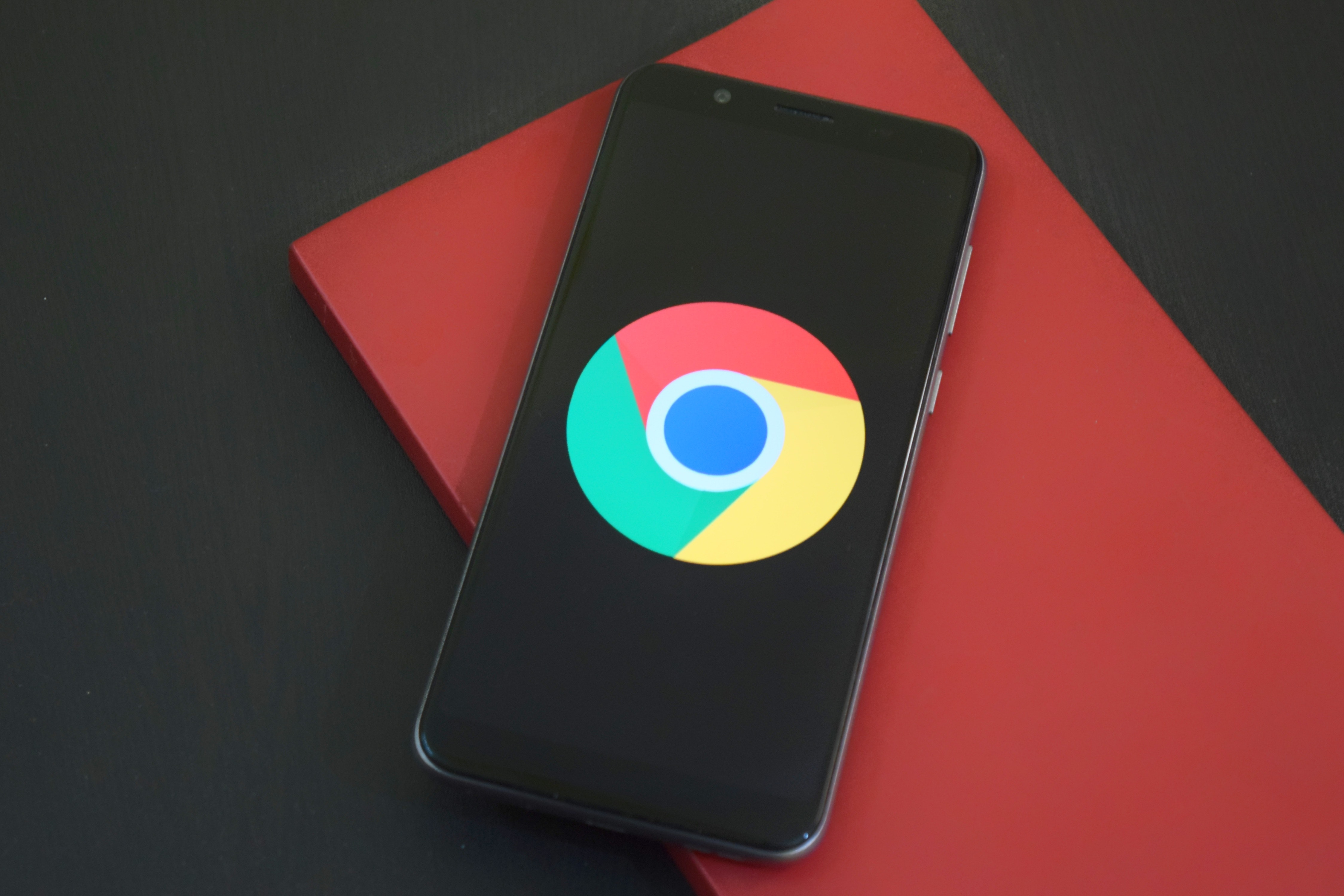 Das Google Chrome-Logo auf einem schwarzen Telefon, das auf einem roten Buch ruht