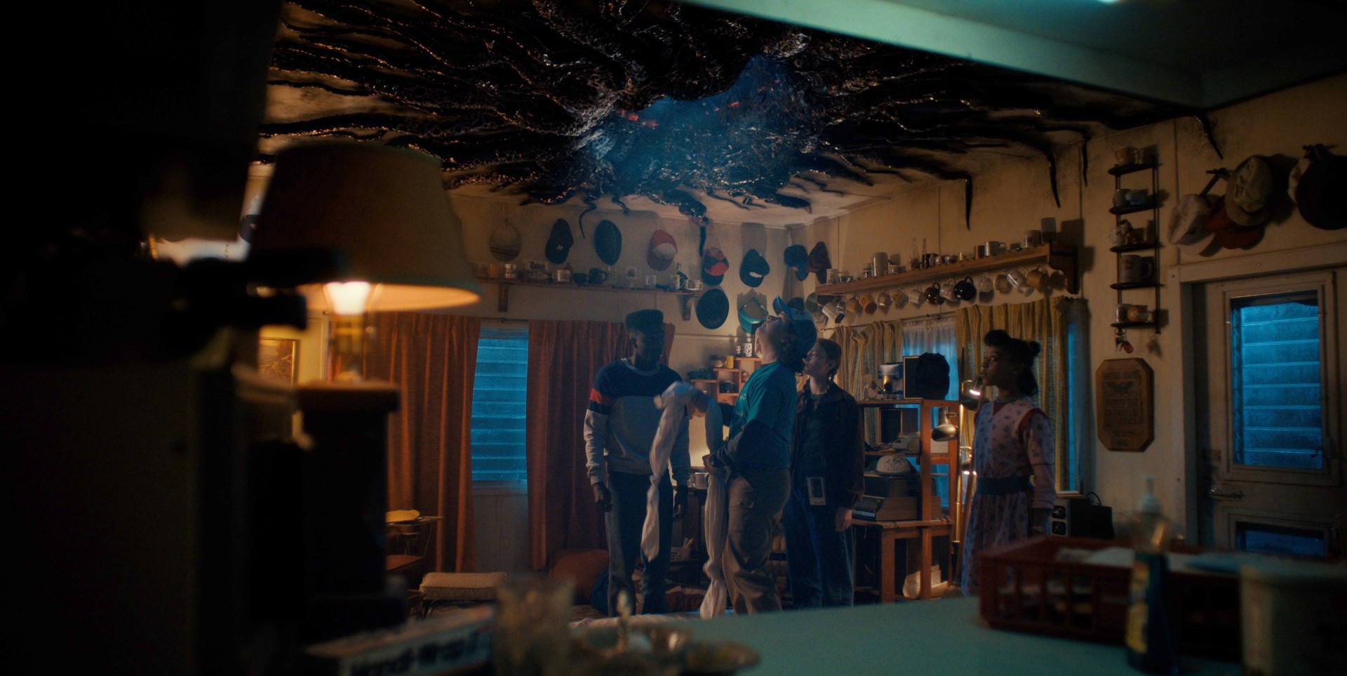 Os personagens de Stranger Things olham para um portal no teto de uma sala.