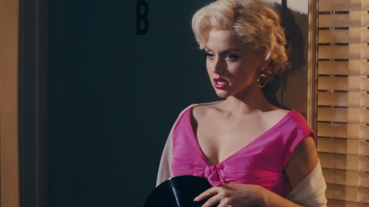 Marilyn Monroe encostada em uma parede e olhando atentamente em Blonde.