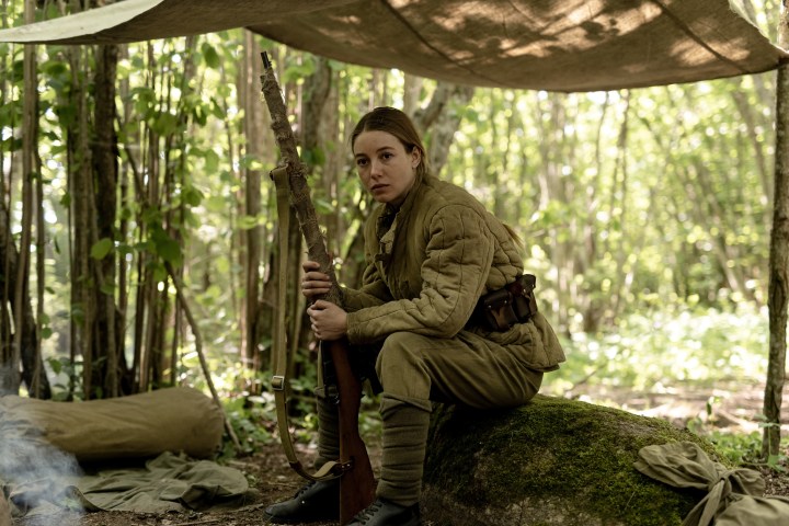 Charlotte Vega sentada e segurando uma arma em cena de Enterro.