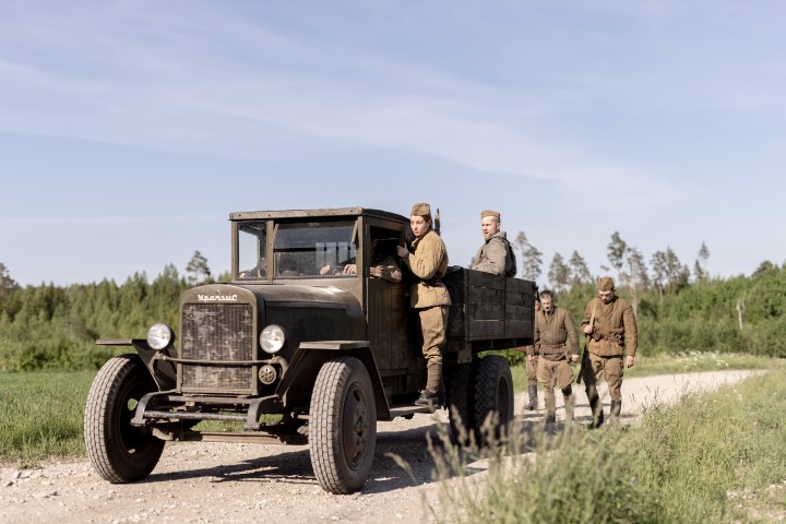 Charlotte Vega and a group of soldiers walk alongside a truck in a scene from Burial.