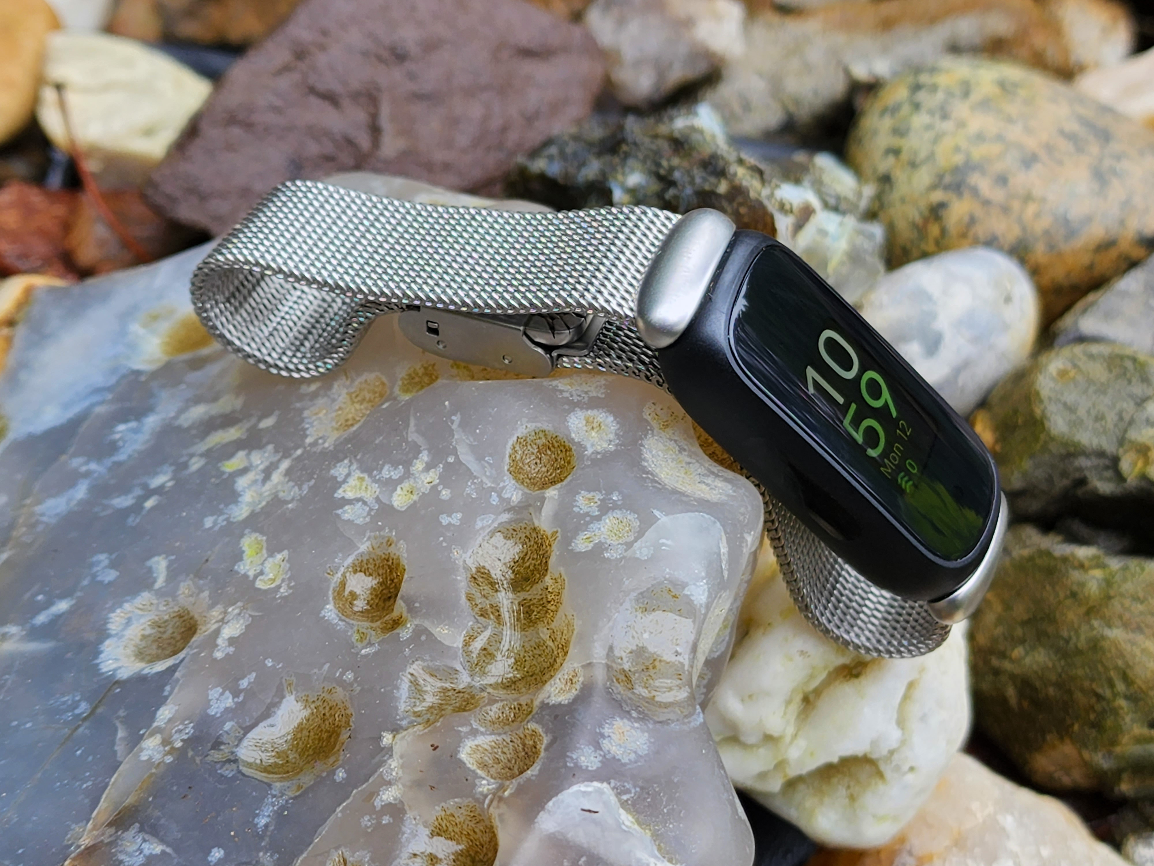 O Fitbit Inspire 3 com banda de aço inoxidável em uma rocha.