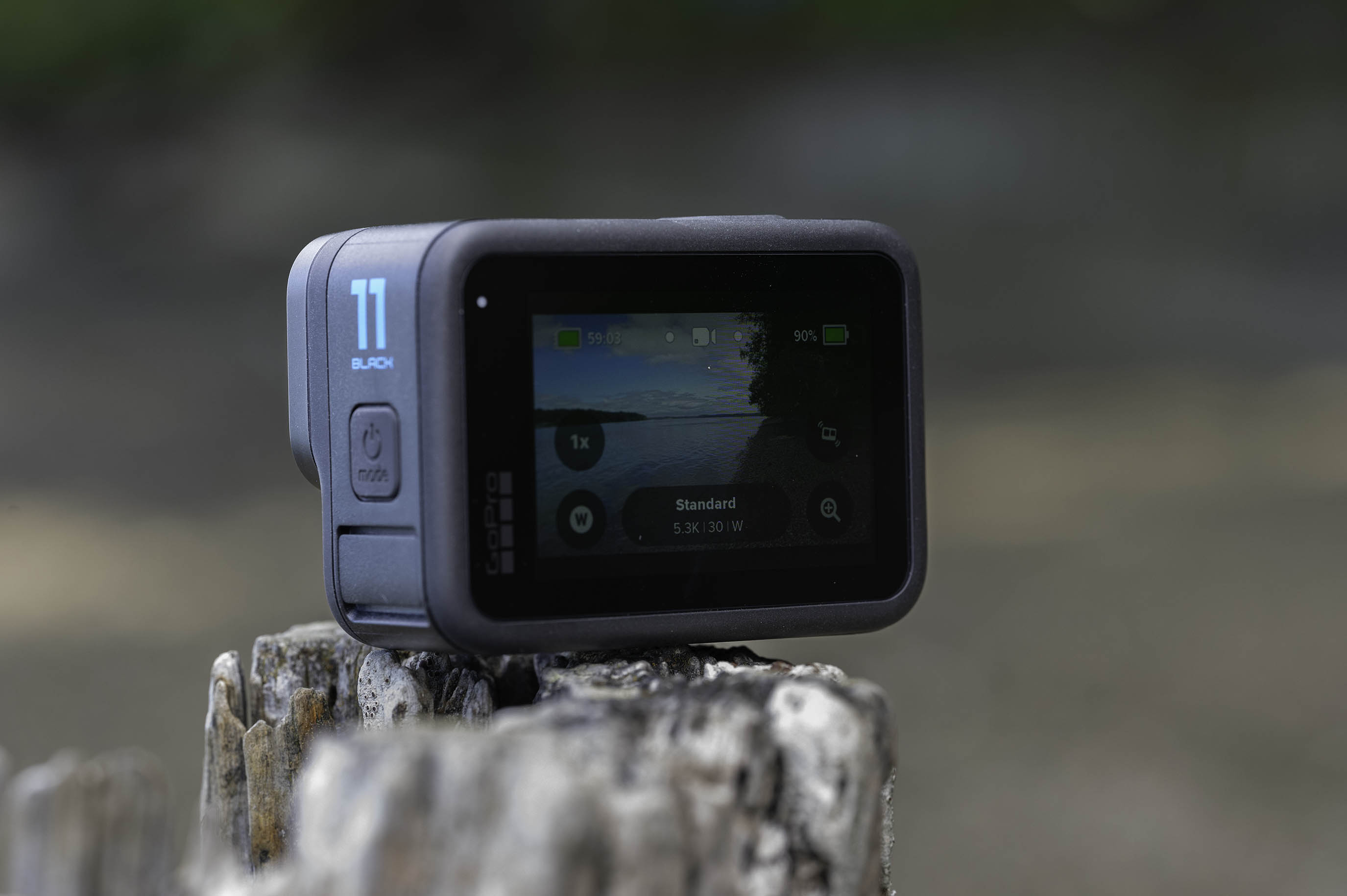 The GoPro Hero 11 Black on an old stump with the screen turned on.