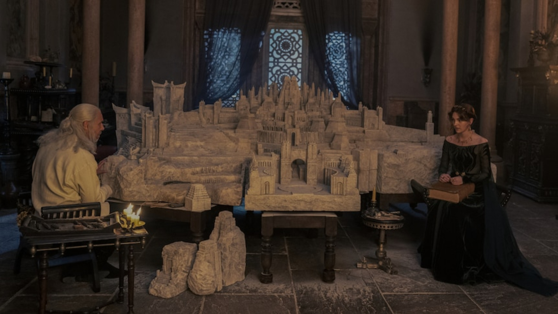 Rei Viserys e Alicent sentados ao lado de seu modelo da Cidade Franca de Valir.