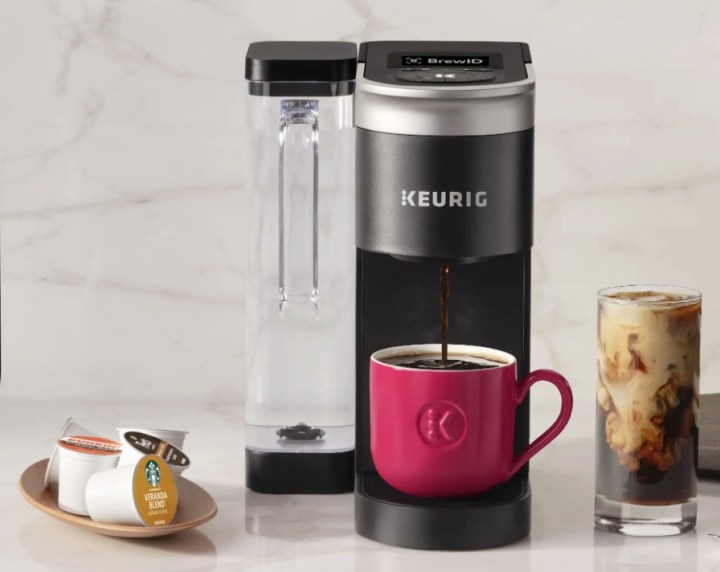A Keurig K-Supreme coffee maker sits on a kitchen counter next to K-Cups and glass of iced coffee.