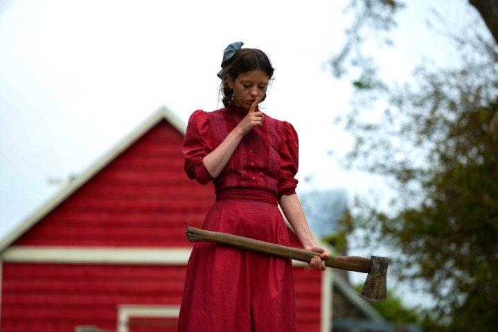 Mia Goth holds an axe while wearing a red dress in A24's Pearl.
