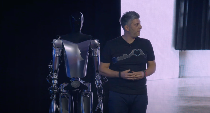 A Tesla employee stands in front of the Optimus robot.