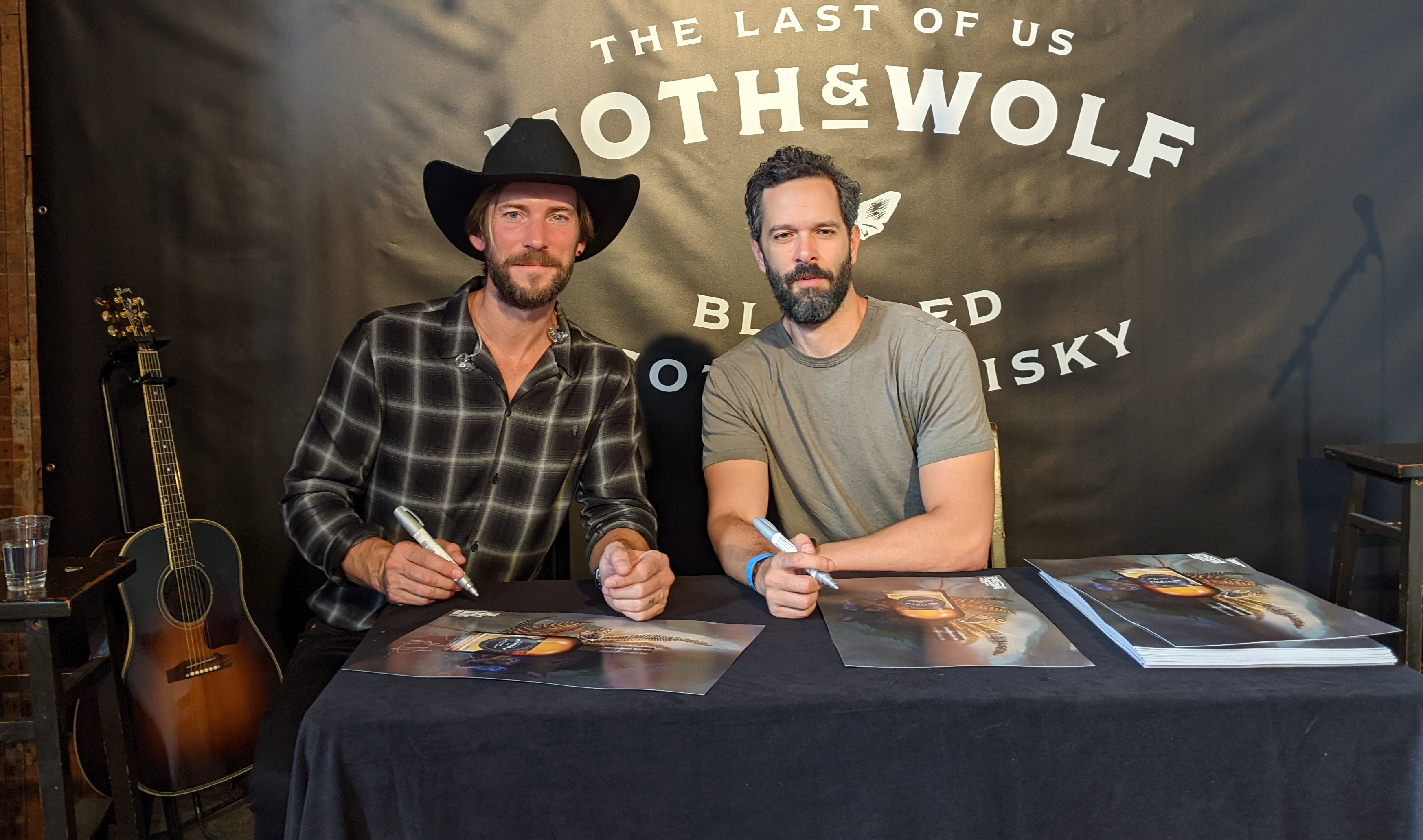 Troy Baker y Neil Druckmann firmando carteles en el evento de degustación de Moth & Wolf. 