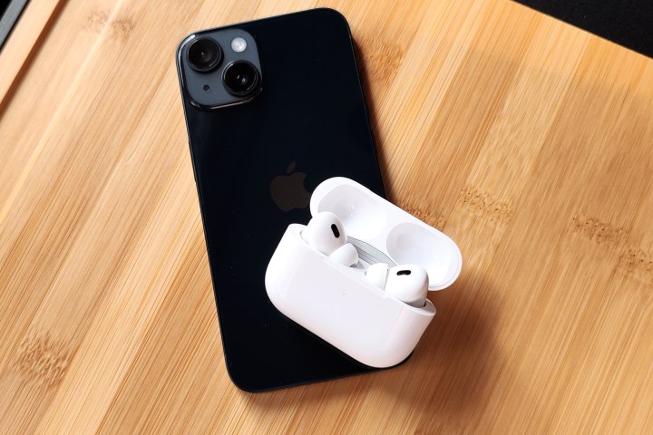 Apple AirPods Pro 2 inside their charging case, sitting on back of an iPhone 14.