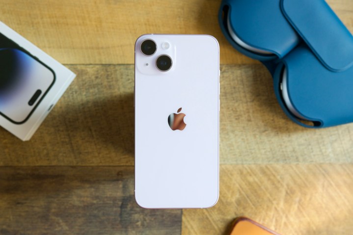 An iPhone 14 sitting on a wood desk.