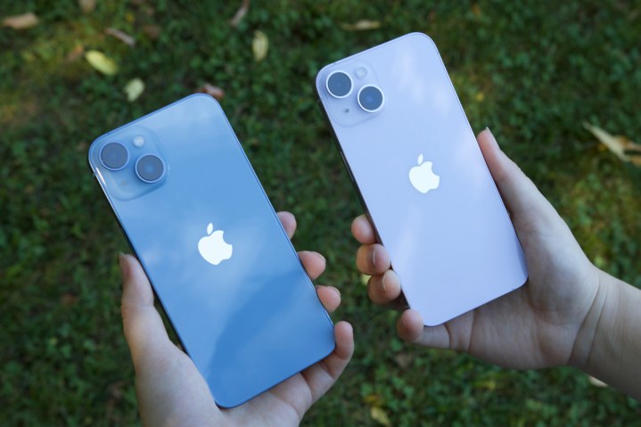 Someone holding a blue iPhone 14 in one hand and a purple iPhone 14 in another hand.