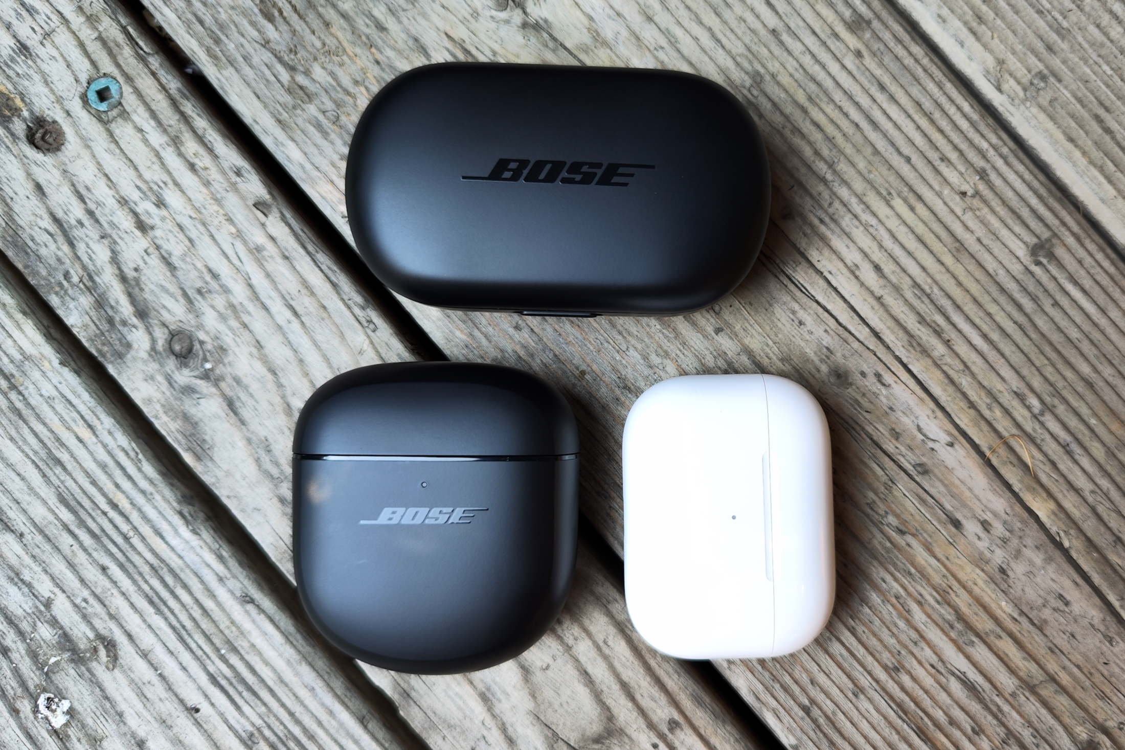 Charging cases for Apple AirPods Pro seen beside charging cases for first and second-gen Bose QuietComfort Earbuds.