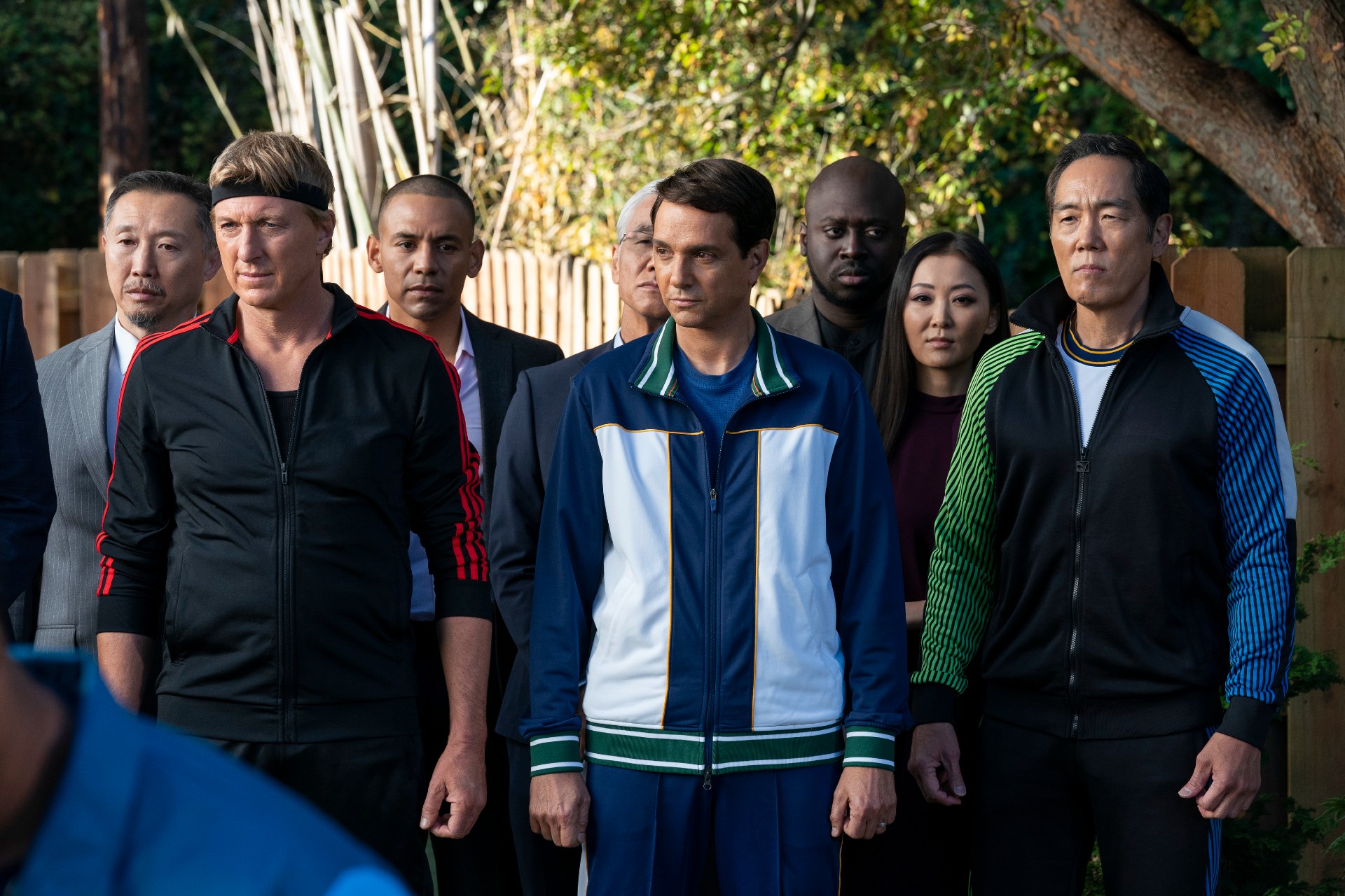 在 Cobr Kai 第五季的一个场景中，威廉·扎布卡、拉尔夫·马奇奥和奥本雄二穿着运动服站立。