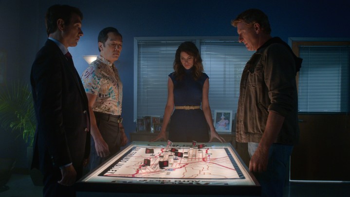 Ralph Macchio, Yuji Okumoto, Courtney Henggeler e William Zabka estão ao redor de uma mesa em uma cena da 5ª temporada de Cobra Kai.