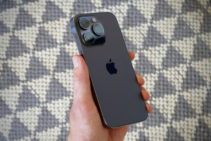 L'iPhone 14 Pro tenuto in una mano d'uomo, visto da dietro.