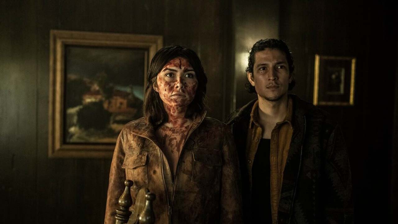 Um jovem casal coberto de sangue em pé em uma casa em uma cena de Tales of the Walking Dead.