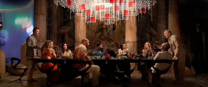 The cast of Glass Onion gather around a table in a scene from the Netflix film.