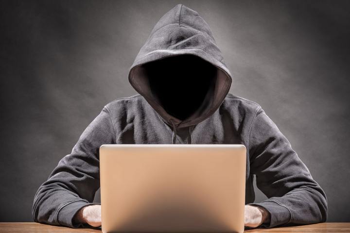 یک هکر بدون چهره در یک هود مشغول تایپ کردن روی لپ تاپ است.