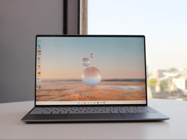 The Dell XPS 13 Laptop sits on a table with a window in the background.
