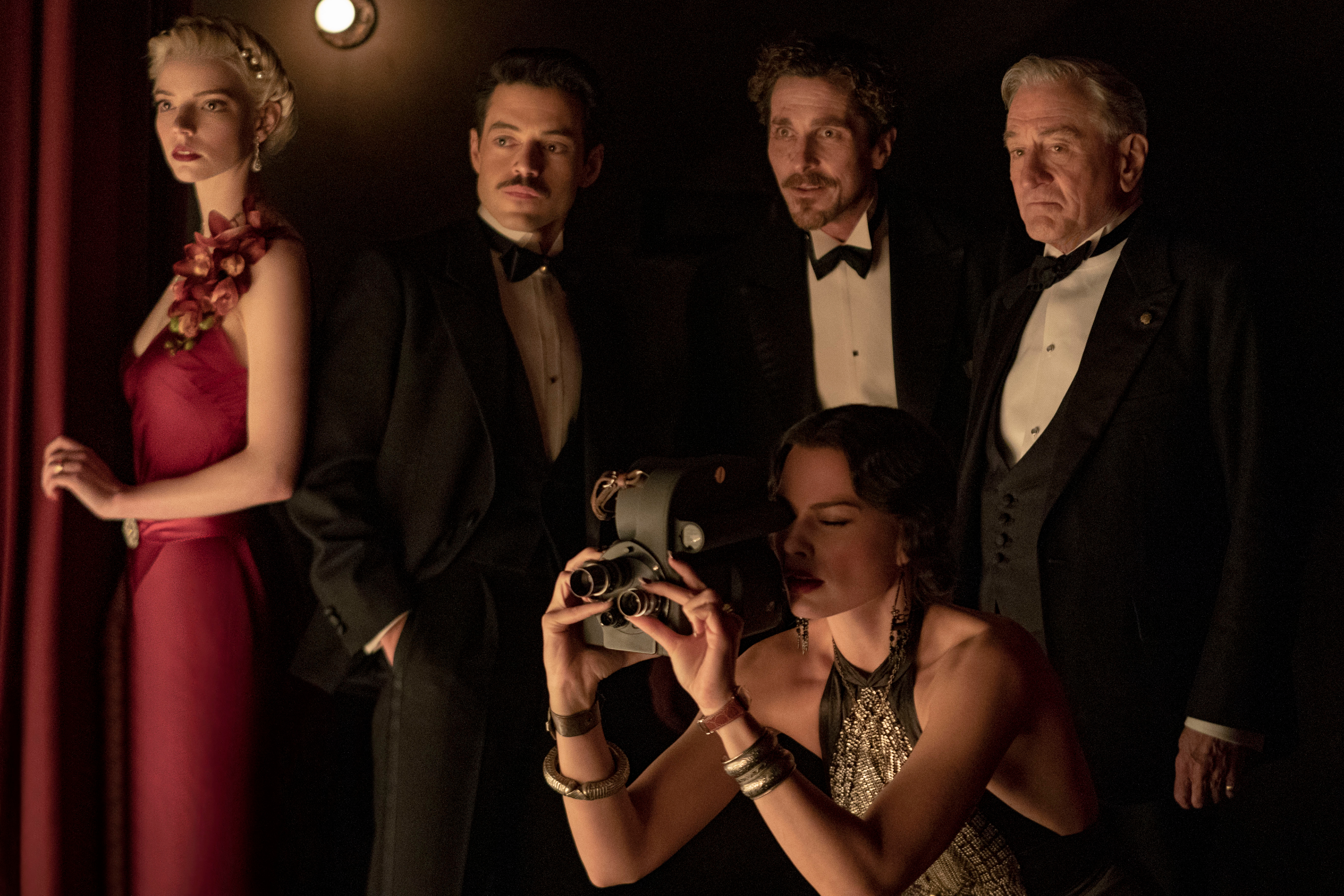 Margot Robbie sostiene una cámara de cine mientras se agacha frente a Anya Taylor-Joy, Rami Malek, Christian Bale y Robert De Niro en Ámsterdam.