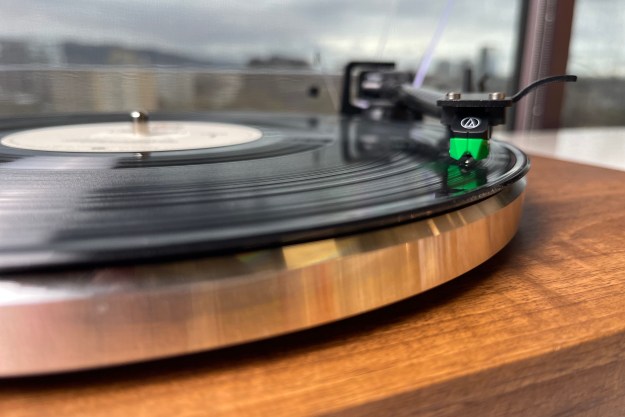 Picture of a green audio technical cartridge settled into the groove of a record on the monolith turntable.