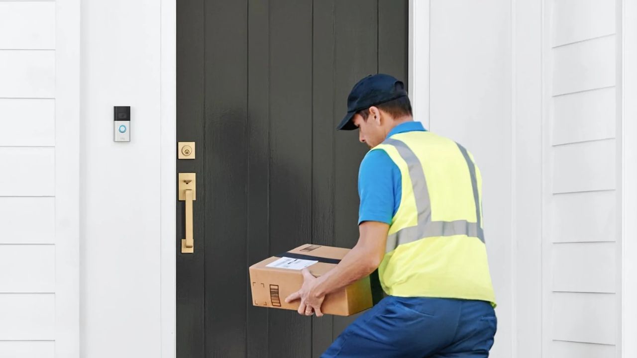 रिंग वीडियो डोरबेल 4 स्थापित होने के साथ एक व्यक्ति एक दरवाजे पर पैकेज वितरित कर रहा है।