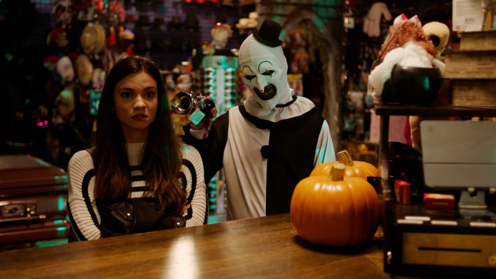 Art the Clown holds a horn to a girl's ear in a scene from Terrifier 2.