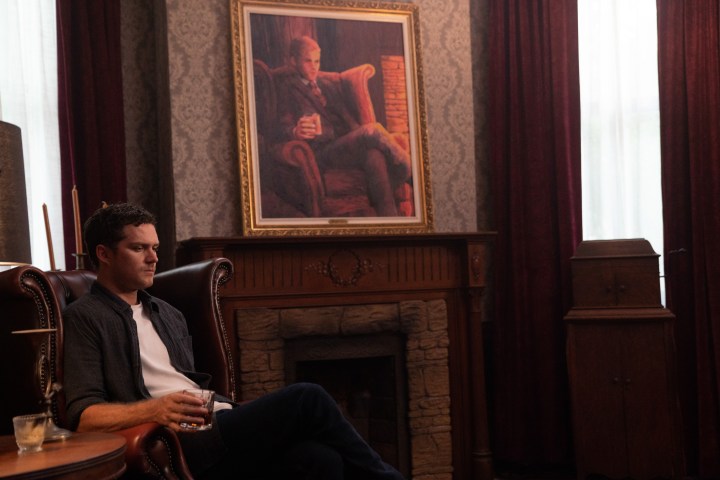 Finn Jones se senta com um copo na mão em uma cena de The Vistor.