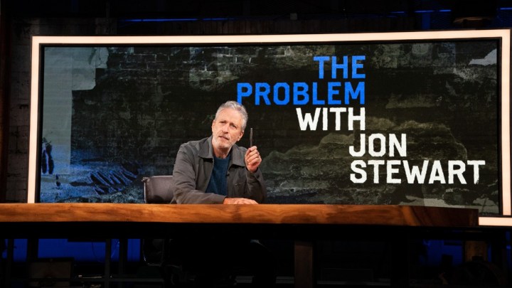 Jon Stewart oturuyor ve kalemini The Problem with Jon Stewart'tan bir sahneye doğrultuyor.