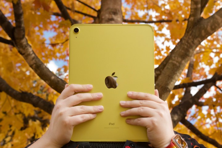 Someone holding the yellow iPad (2022) in front of trees with orange, yellow leaves.