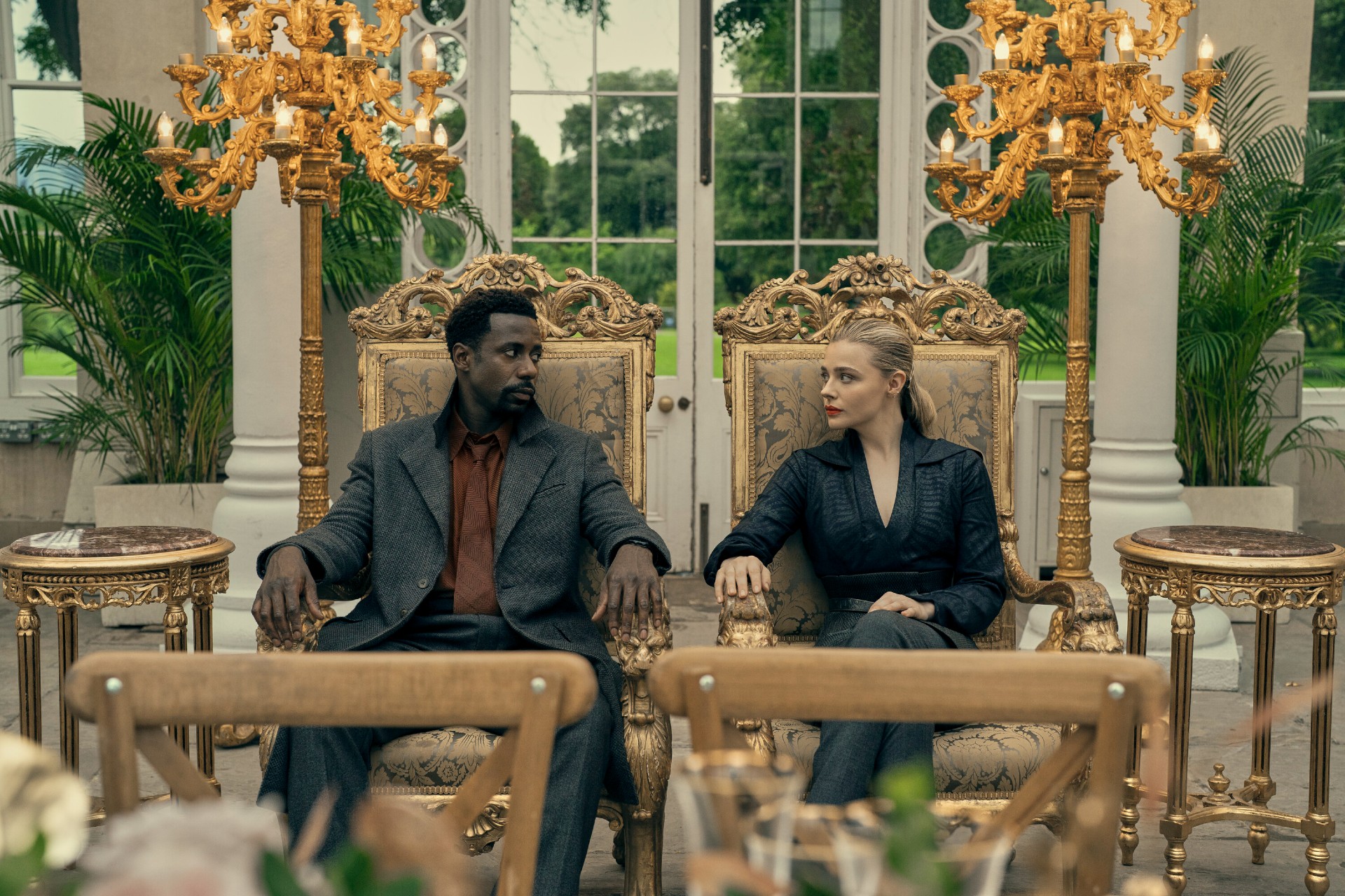 Gary Carr and Chloe Grace Moretz stare at each other while seated in a scene from The Peripheral.