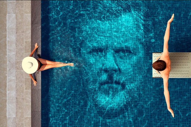 A man and a woman sit by a pool with an image of a man's face in the water.
