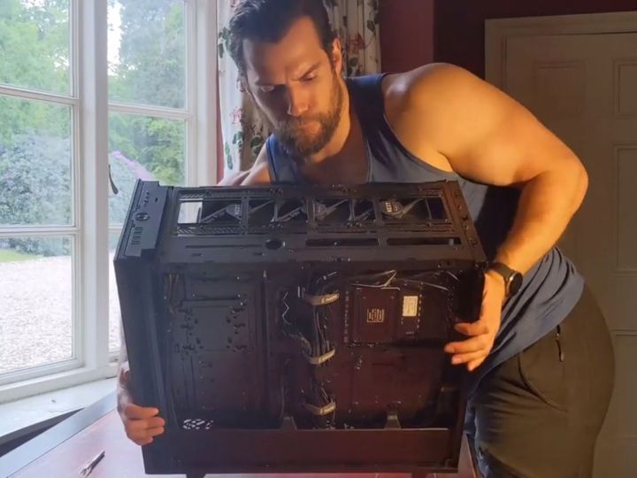Henry Cavill lifting a gaming PC off a table.