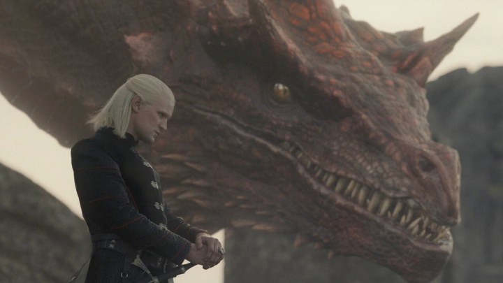 Деймон стоит рядом со своим драконом в Доме Дракона.