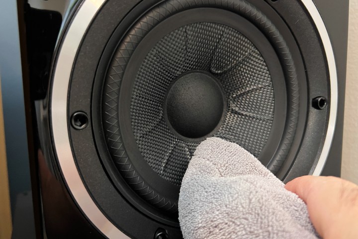 A speaker being wiped with a microfiber cloth.