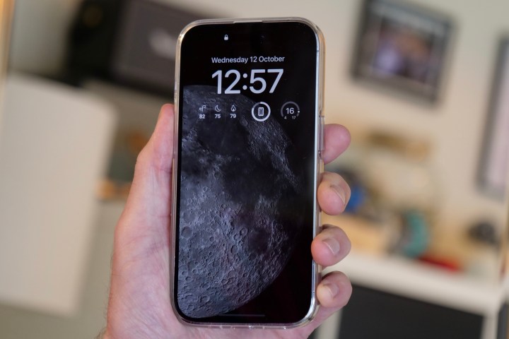 iPhone 14 Pro showing the always-on moon screen, held in the hand of a man.