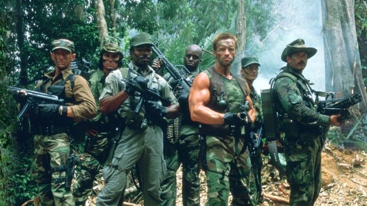 The cast of Predator poses with their guns in the jungle.