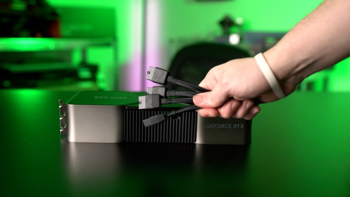A placa de vídeo RTX 4090 em uma mesa ao lado de um conjunto de cabos na mão.