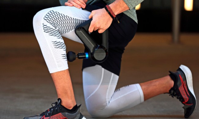 A man kneeling and using a Theragun Elite handheld percussive massage device on his calf.